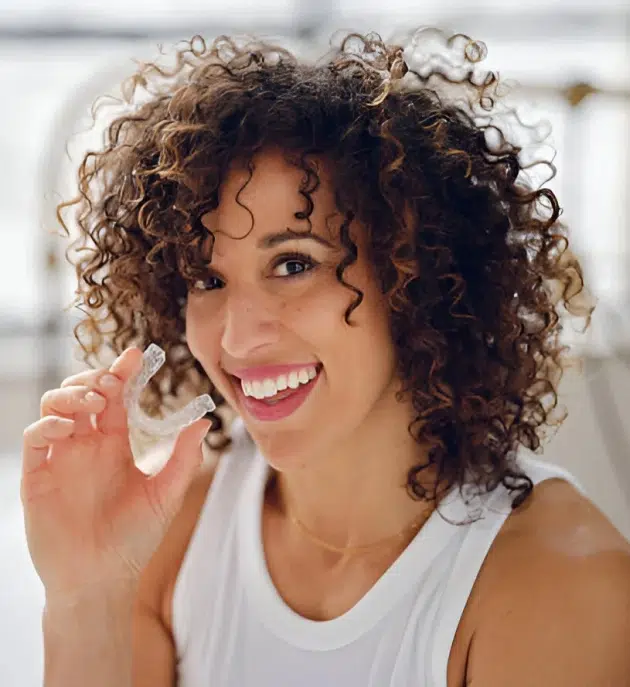 Woman smiling while holding a clear Invisalign aligner.